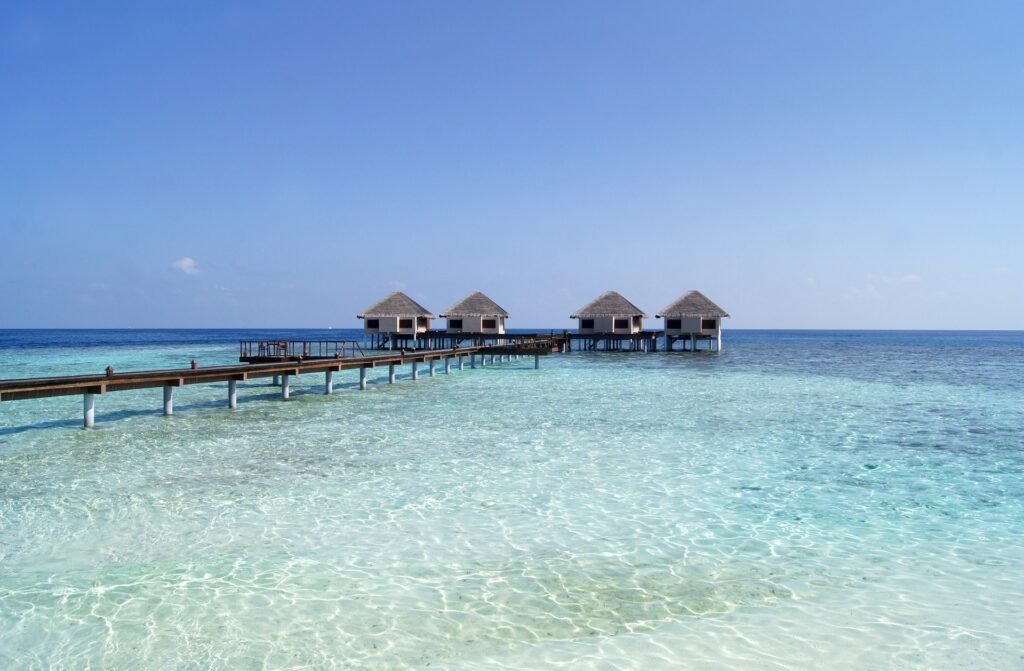 A serene view of the Maldives, featuring clear turquoise waters, white sandy beaches, and overwater bungalows under a bright blue sky.